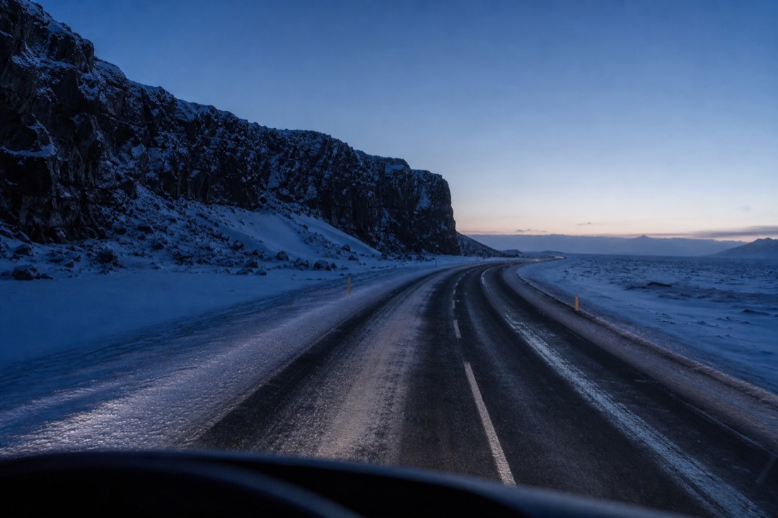 Tour coach headlights sweeping a snow-banked Route 1 before dawn, empty road ahead