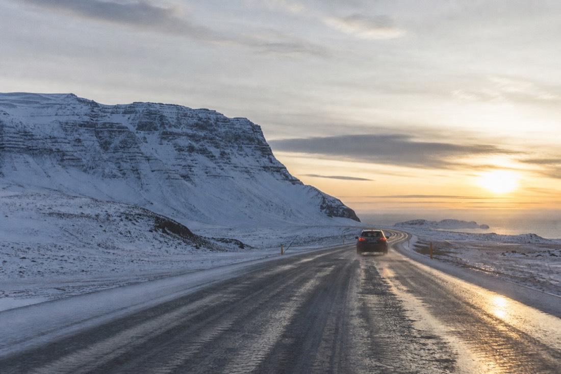 Cleared and gritted road through snowy southwest Iceland under a low winter sun, one car
