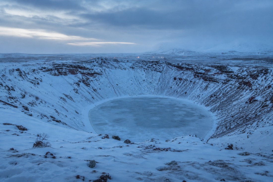 Kerid crater under snow, red rim showing through the white and the lake frozen below