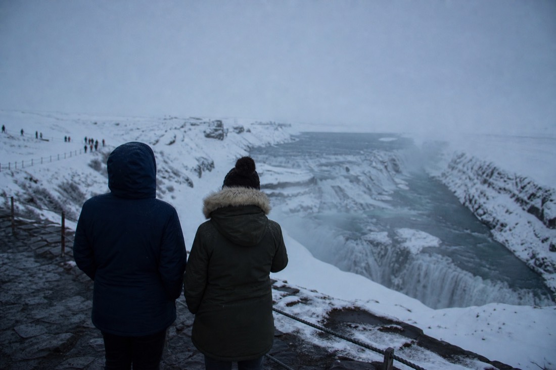 Visitors seen from behind at a snowy Golden Circle viewpoint in flat winter light