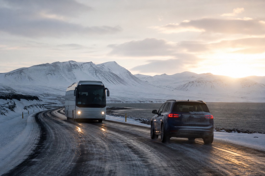 Hire car and tour coach passing on a snow-lined Ring Road in low arctic sun