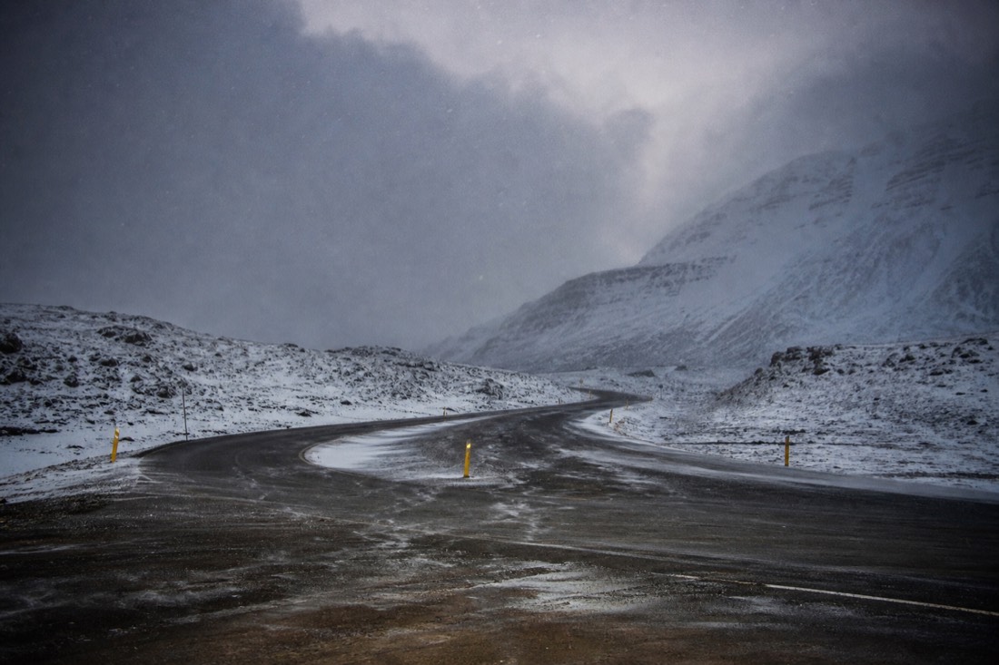 Snowfall closing in over an empty road junction in south Iceland, marker posts and low cloud