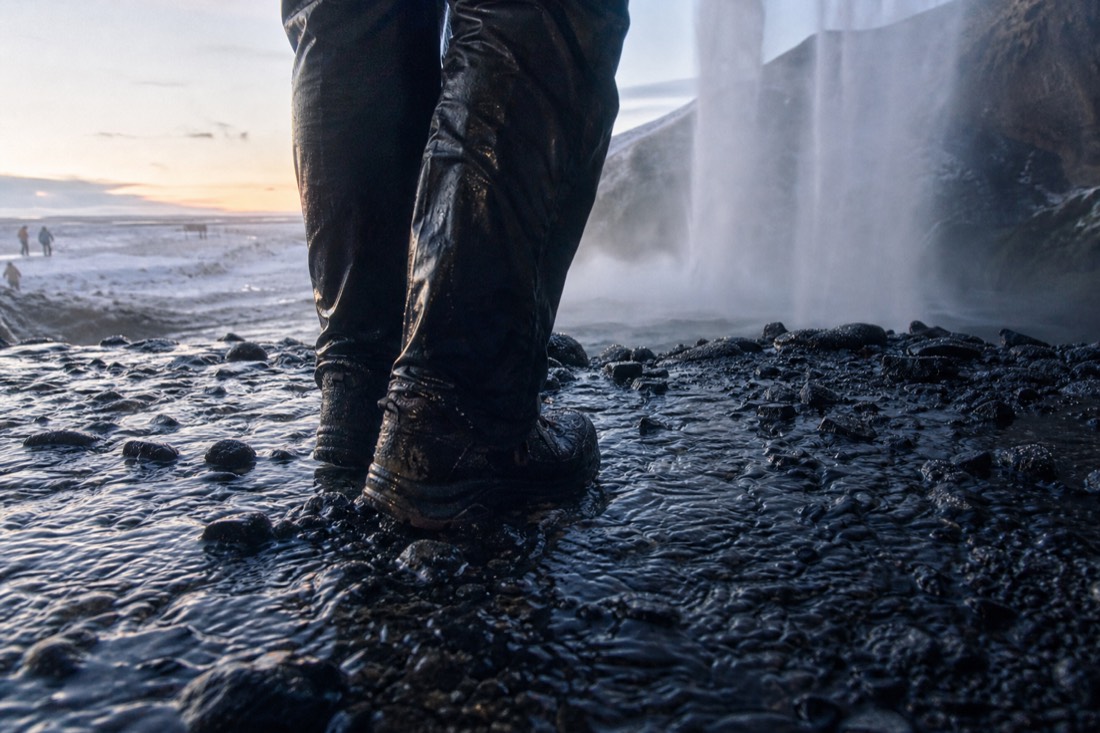 Soaked trousers and boots in the spray at the base of Seljalandsfoss, cropped low, no face