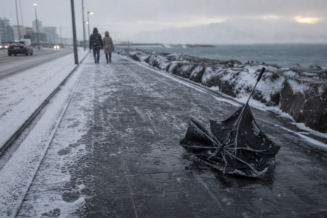 Inverted broken umbrella on a snowy Reykjavik pavement in strong wind, overcast light