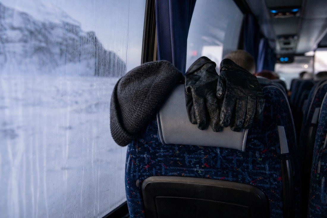 Wet gloves and a wool hat drying on a coach seat, window fogged with snow outside