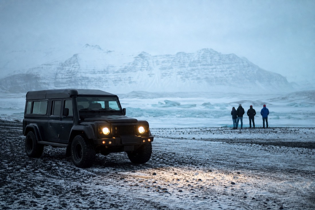 Super jeep waiting at a snowy meeting point near Jokulsarlon, headlights on in flat light