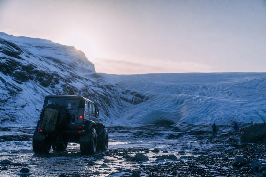 Modified super jeep crossing rough moraine track below a glacier tongue in low winter sun